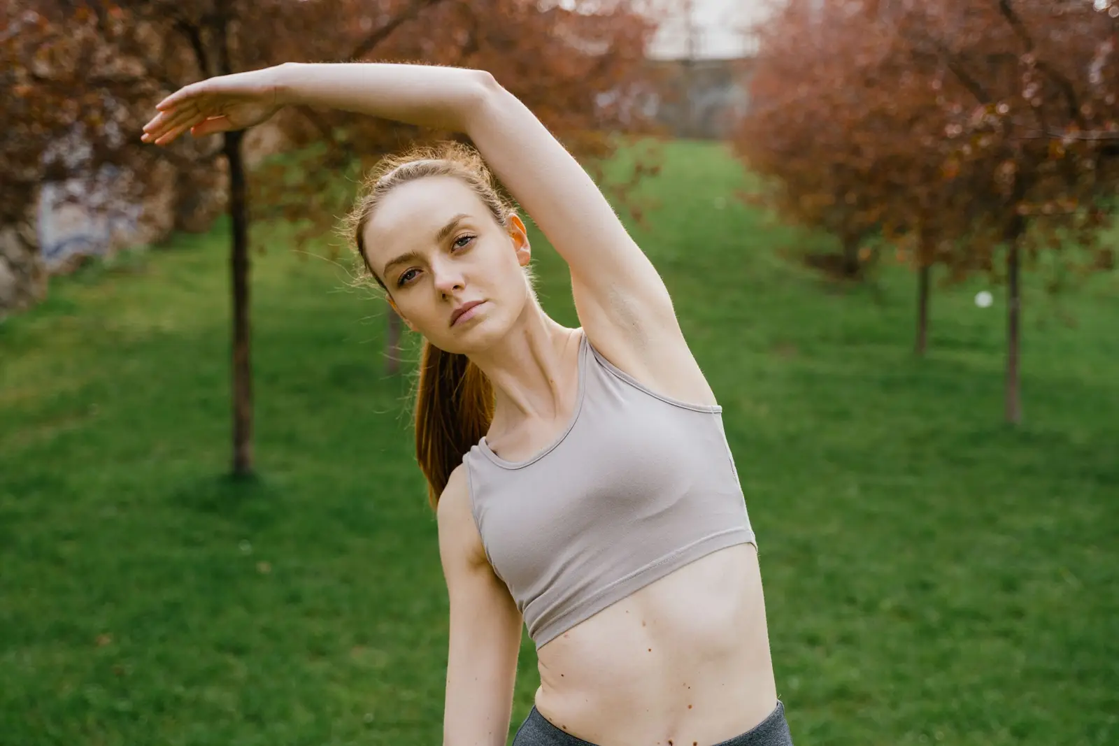 Woman doing a standing side stretch on the grass in a park
